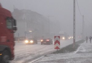 pojazdy jadące po drodze podczas gdy pada intensywny śnieg