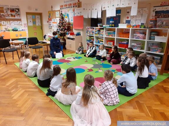 Dzielnicowa rozmawiająca z dziećmi w sali przedszkolnej.