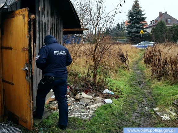 policjant w mundurze stoi przy altance działkowej, w tle po prawej stronie radiowóz