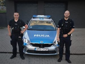 Dwóch policjantów w mundurach stojących przed oznakowanym radiowozem