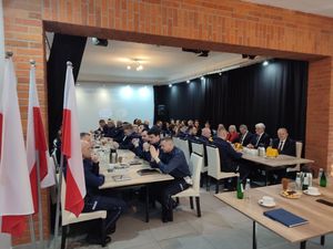 Na zdjęciu widzimy kilkudziesięciu policjantów siedzących przy stołach na odprawie rocznej.