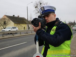 Na zdjęciu widzimy policjanta Ruchu Drogowego mierzącego prędkość pojazdom.