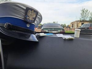 Na zdjęciu widzimy kokpit samochodu na którym położona jest czapka policyjna Ruchu Drogowego, tester narkotykowy oraz woreczki strunowe z zawartością środków odurzających.