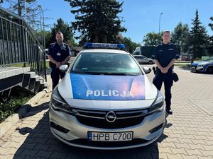 Na zdjęciu widzimy dwóch policjantów stojących po dwóch stronach radiowozu.