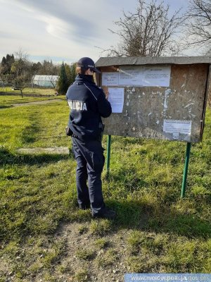 Na zdjęciu umundurowany funkcjonariusz zawiesza ulotkę na tablicy ogłoszeń.